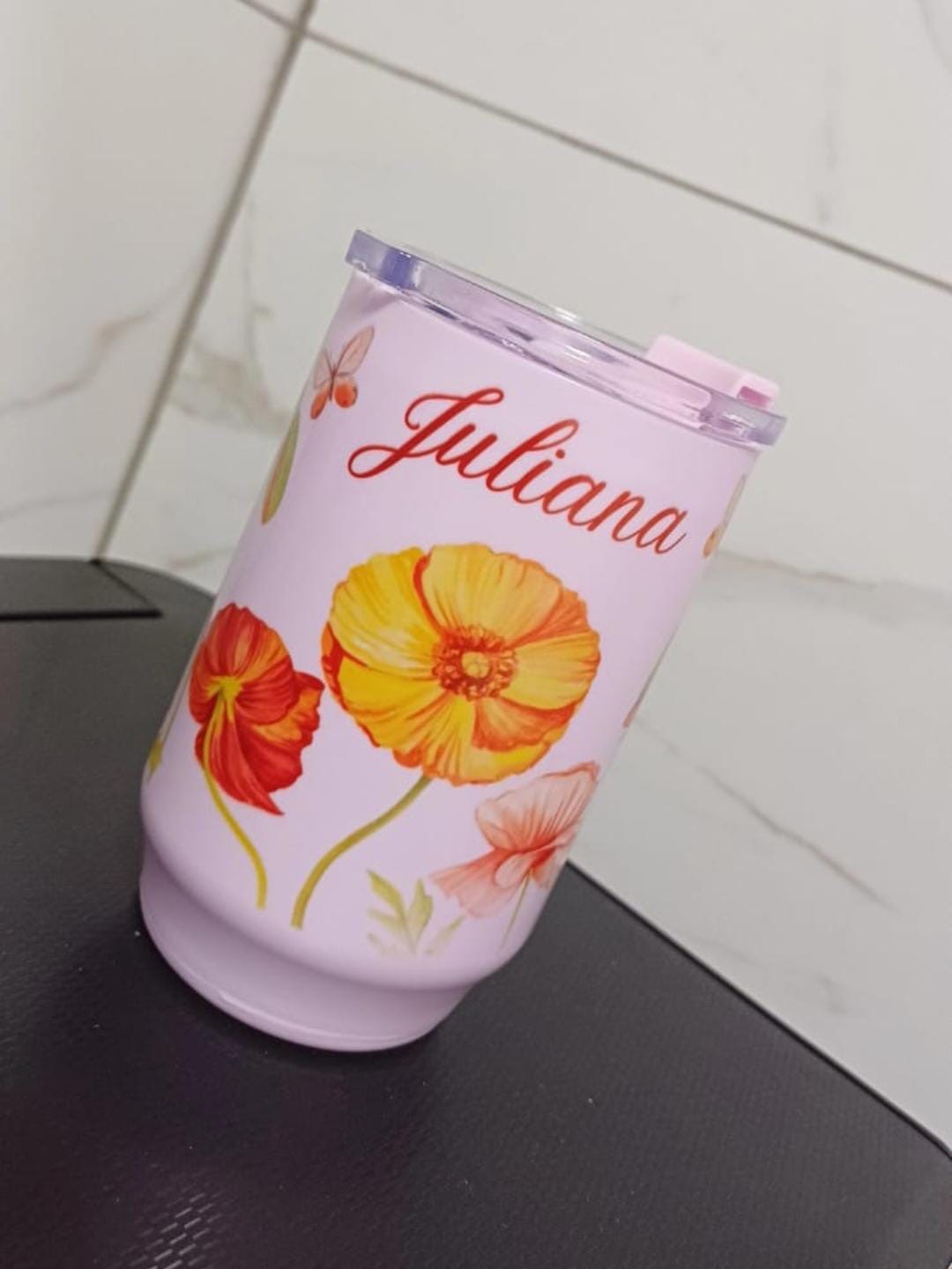 Copo térmico lilás com tampa transparente, flores em aquarela amarelas e vermelhas, borboleta e o nome Juliana